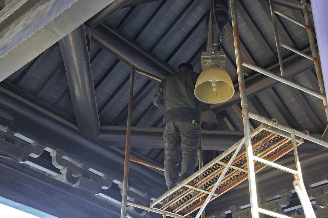 5、	工人站在脚手架子上，准备给亭内顶部装上挂大红灯笼的滑轮和铁吊钩。