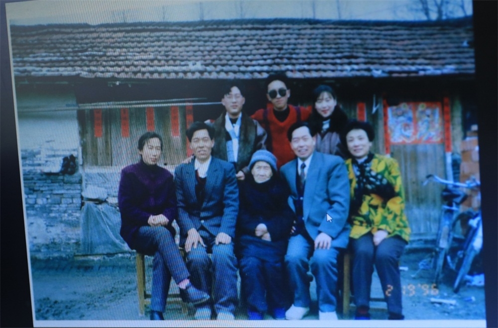 1996年春节徐老和妻儿回家在老屋前照的全家福，身后就是原来的简陋平房。
