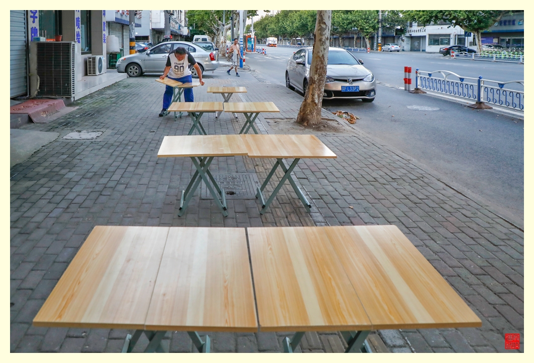 志愿者在店铺门口的人行道上摆放桌凳。