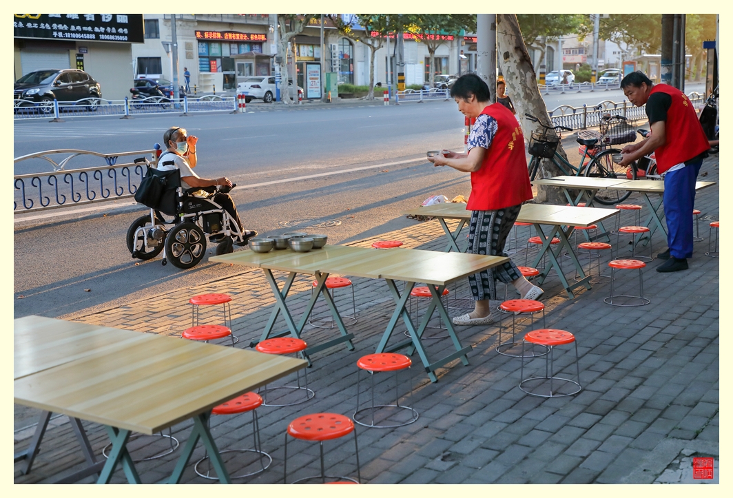 志愿者在招呼路过的坐轮椅的老人来吃粥。